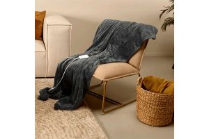 Donkergrijze elektrische fleece deken van Silvana, gedrapeerd over een beige stoel in een warme woonkamer met mand en vloerkleed.