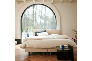 Auping Original boxspring in lichte slaapkamer met groot rond raam en neutrale tinten