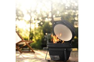 Kamado BBQ met open deksel en brandend vuur in een zonnige tuinsetting.
