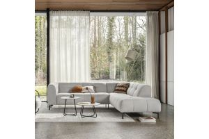 Lichtgrijze hoekbank met afgeronde vormen in moderne woonkamer, voor groot raam met witte gordijnen en twee ronde bijzettafels.