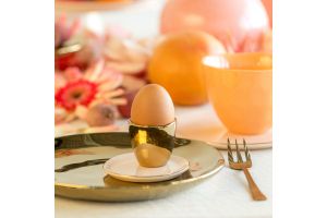 Gouden eierdopje met ei op bord in kleurrijke en sfeervolle tafelsetting