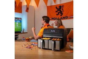 Twee supporters in oranje juichen voor de televisie tijdens een voetbalwedstrijd, met een airfryer op tafel als onderdeel van de WK-actie van Home Center en Kapenga Wonen.