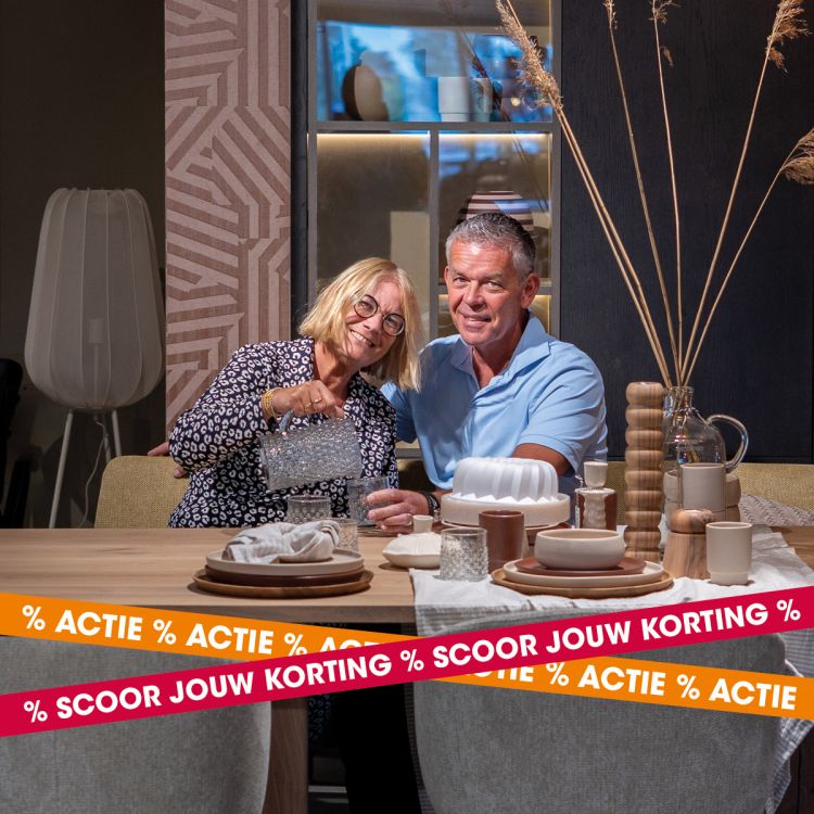Echtpaar zit aan een sfeervol gedekte eettafel in een warme woonomgeving tijdens de pre-opruiming van Kapenga Wonen, met de tekst Scoor jouw korting.