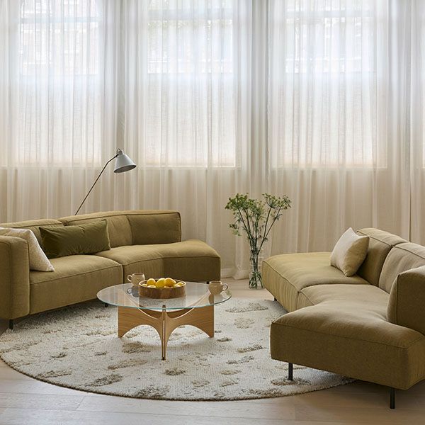 Gelderland 6400 banken in een moderne woonkameropstelling met lage armleuningen, groene kussens en een ronde vloerkleed met glazen salontafel.