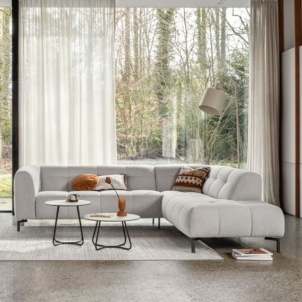 Moderne witte hoekbank in lichte woonkamer met grote ramen, ronde salontafels en sfeervolle accessoires