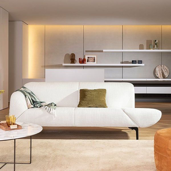 Moderne woonkamer met een witte designbank van Jori, groene sierkussen, plaid en strakke wandkasten met ingebouwde verlichting.