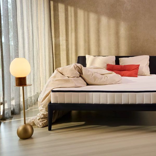 Auping bed en matras in moderne slaapkamer met beige beddengoed en design vloerlamp