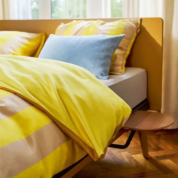 Auping Original bed met geel gestreept dekbedovertrek en lichtblauw kussen in moderne slaapkamer setting.
