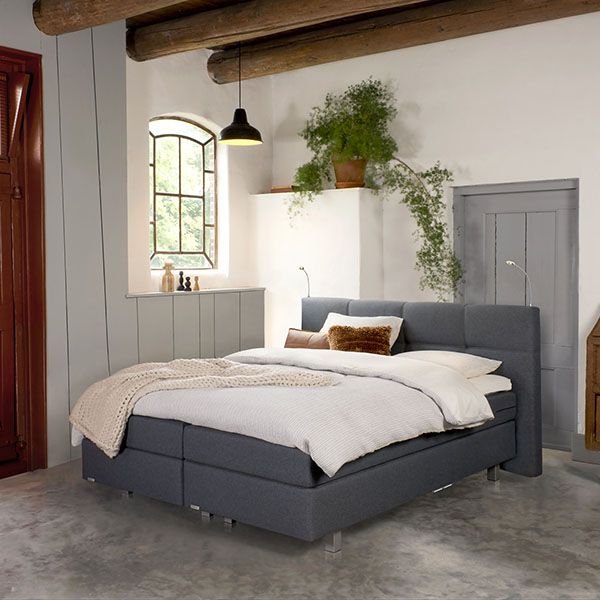 Donkergrijze boxspring met gestoffeerd hoofdbord in sfeervolle landelijke slaapkamer met houten balken en grote ramen