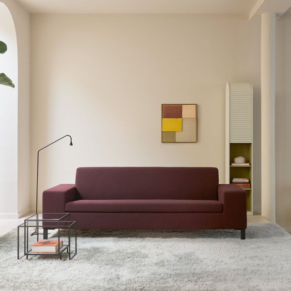 Moderne bordeauxrode bank in minimalistisch interieur met lichte muren, vloerlamp en bijzettafels