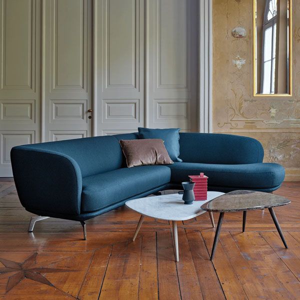 Blauwe, organisch gevormde hoekbank in stof met sierkussens en twee salontafels op een houten vloer in een klassieke interieursetting