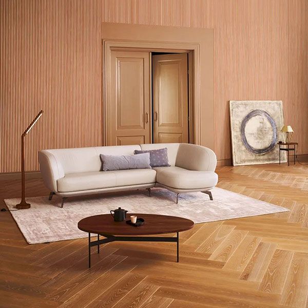 Leolux Flint hoekbank in lichte stof met afgeronde vormen, geplaatst in een warme woonkamer met houten vloer, vloerkleed en ovale salontafel.