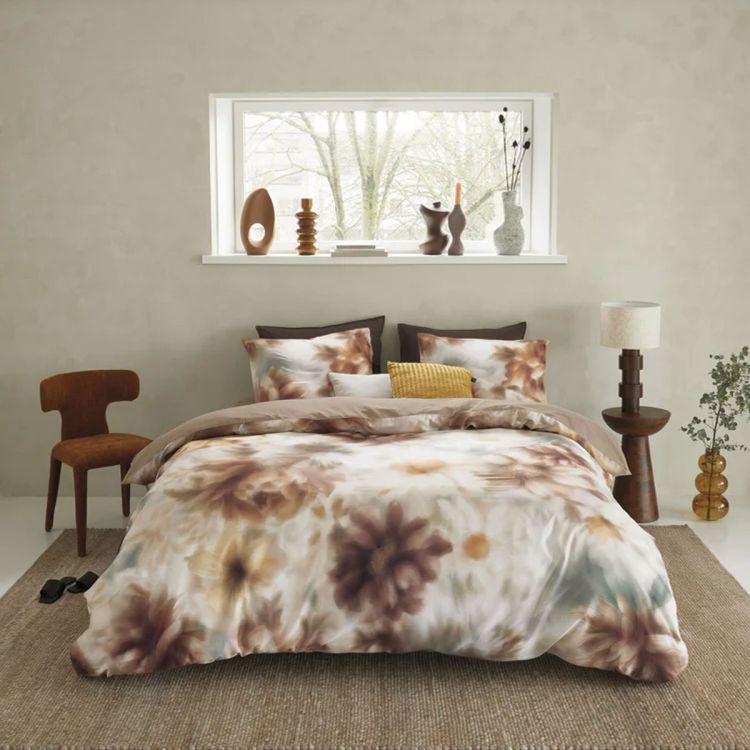 Sfeervol opgemaakt bed met bloemendessin dekbedovertrek in warme aardetinten, gestyled in een rustige slaapkamer met houten meubels en decoratie op de vensterbank