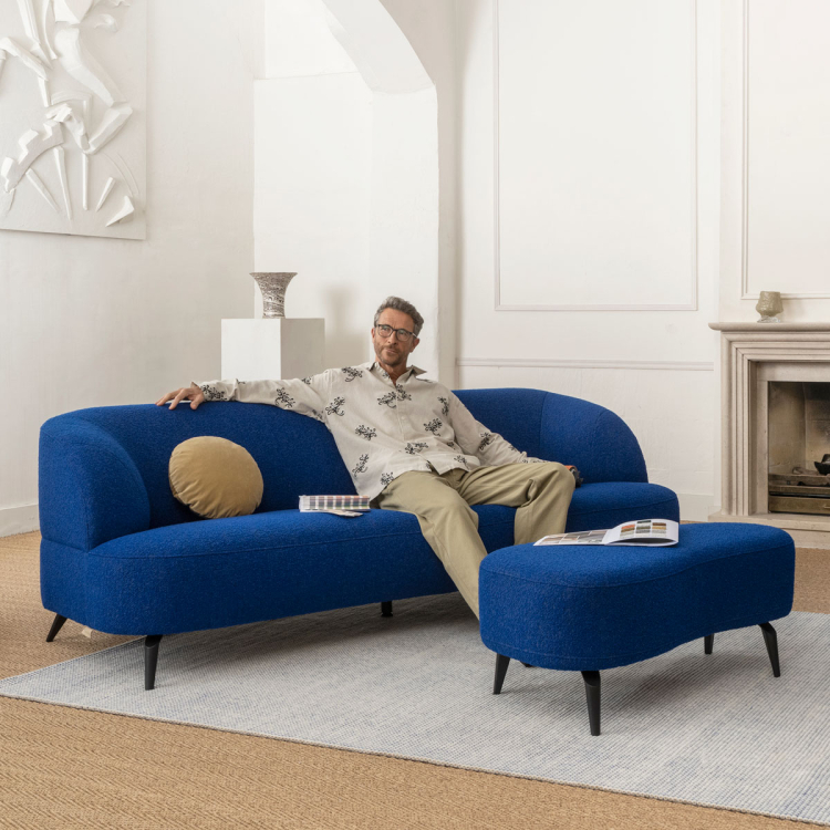 Man ontspannen zittend op een moderne blauwe designbank met bijpassende hocker in een stijlvolle woonkamer