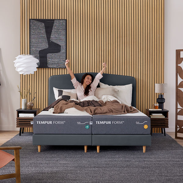 Persoon ligt ontspannen op Tempur matras en strekt zich uit in moderne slaapkamer met houten wand en stijlvolle inrichting