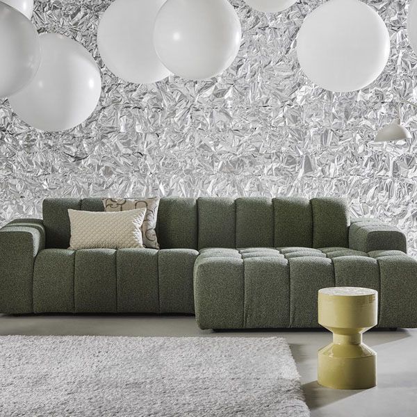 Groene modulaire bank in een modern interieur met witte hanglampen, zilveren textuurwand en zacht vloerkleed