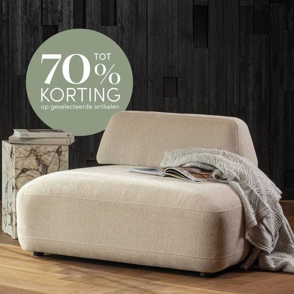 Beige chaise longue van WOOOD in een modern interieur, met zachte stoffering, afgeronde vormen en een plaid met boek erop, afgebeeld met een groene badge tot 70% korting.