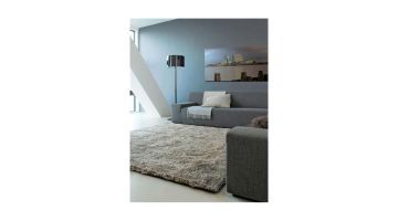 Een woonkamer met een grijs CSrugs Sauvage vloerkleed, gecombineerd met een grijze bank, wandlamp en modern wandpaneel in een lichte ruimte.