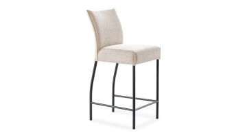 schuinaanzicht beige stoffen barkruk van pronto Wonen. De kruk heeft een stoffen zitting en rugleuning en zwart metalen poten. De achterpoten zijn iets gebogen.