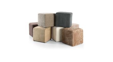 Verschillende INHOUSE poefjes Hebera in warme neutrale kleuren zoals beige, crème, bruin en grijs. De poefs zijn kubusvormig en hebben elk een andere stofstructuur, waaronder ribfluweel, bouclé en velours.
