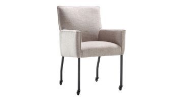 Eetkamerstoel Mianta van INHOUSE in beige stof, met armleuningen en zwart metalen poten op wieltjes, schuin van voren gefotografeerd.