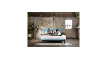 Lifestylefoto van Avek Stiel bed met blauw hoofdbord, vrouw liggend met laptop.