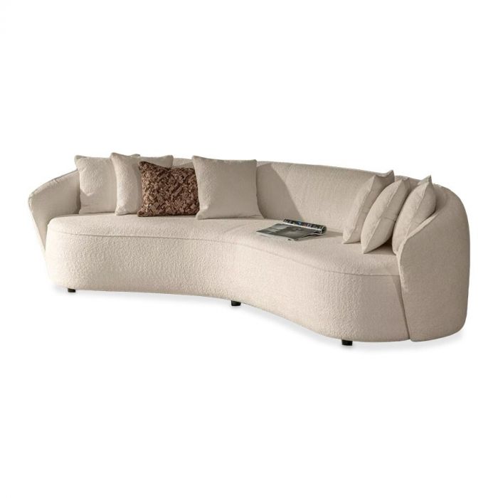 Gebogen lichtbeige bank met meerdere bijpassende kussens en één contrasterend decoratief kussen, met een modern en stijlvol ontwerp.