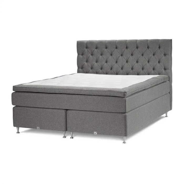Grijze boxspring Victoria Continental met gecapitonneerd hoofdbord, dubbele matrassen en metalen pootjes, schuin van voren gefotografeerd.