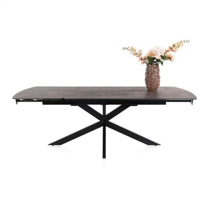 Vooraanzicht van de Henders & Hazel Pavalon uitschuifbare eettafel in roestkleur met zwarte spinpoot en bloemenvaas op het blad.