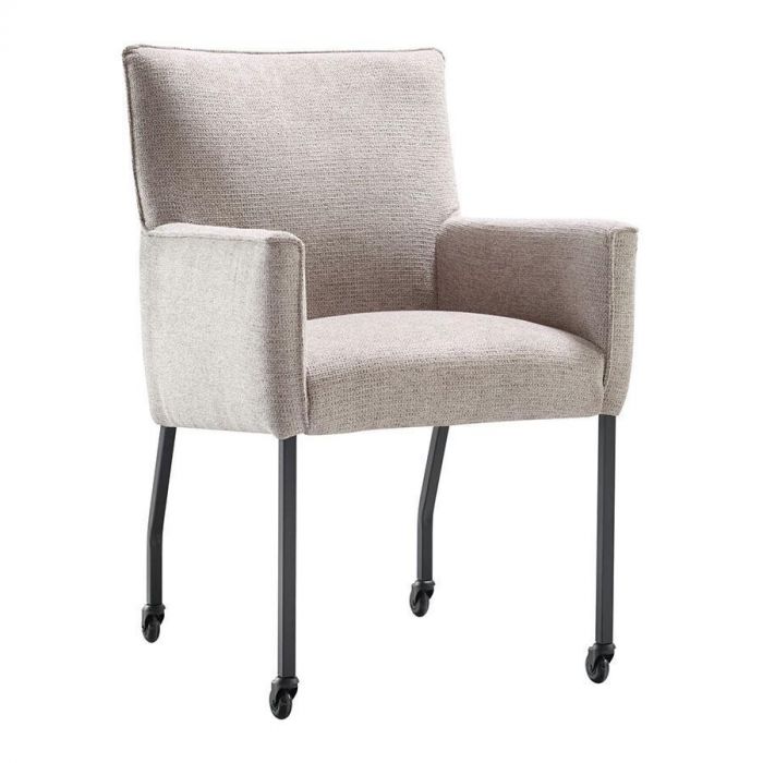 Eetkamerstoel Mianta van INHOUSE in beige stof, met armleuningen en zwart metalen poten op wieltjes, schuin van voren gefotografeerd.