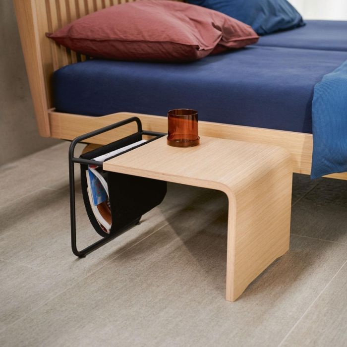 Auping Noa nachttafeltje van licht eikenfineer met zwart stalen frame en vilten magazinehouder naast houten bed