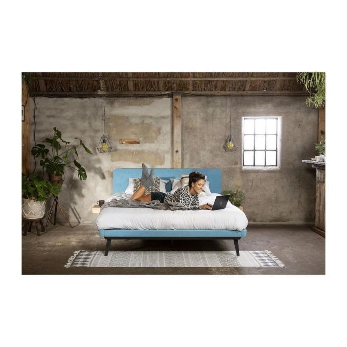 Lifestylefoto van Avek Stiel bed met blauw hoofdbord, vrouw liggend met laptop.
