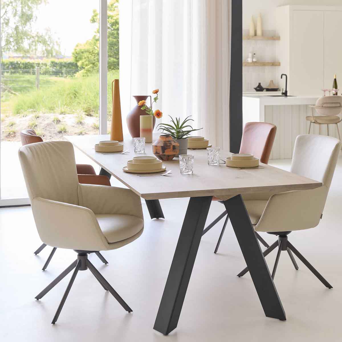Ovale eettafel met donker blad en moderne kuipstoelen in leer en stof van Bert Plantagie, in lichte eetkamer met designlamp en open wandplanken