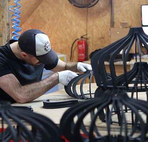 Ambachtsman van Blij Design met pet en handschoenen monteert zwarte lampenonderdelen in Nederlandse werkplaats met houten wanden.