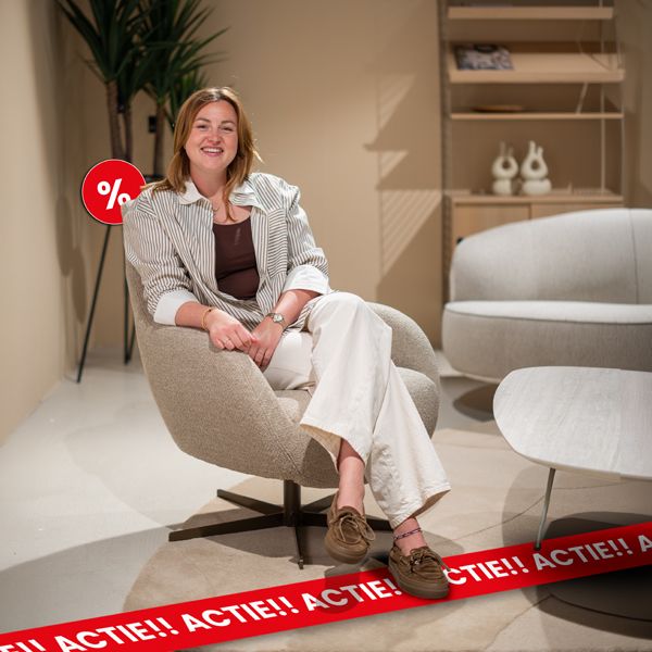 Lachende vrouw presenteert een stijlvolle designfauteuil tijdens de Home Opruiming met extra voordeel op meubels en woonaccessoires.