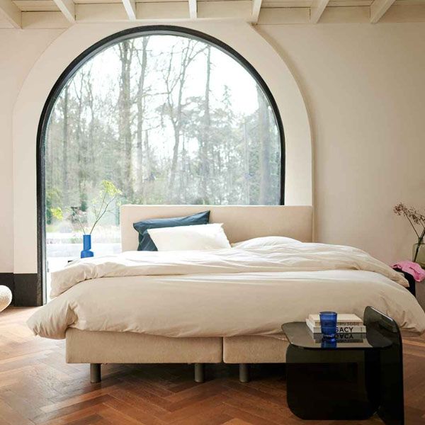 Auping Original boxspring in lichte slaapkamer met groot rond raam en neutrale tinten