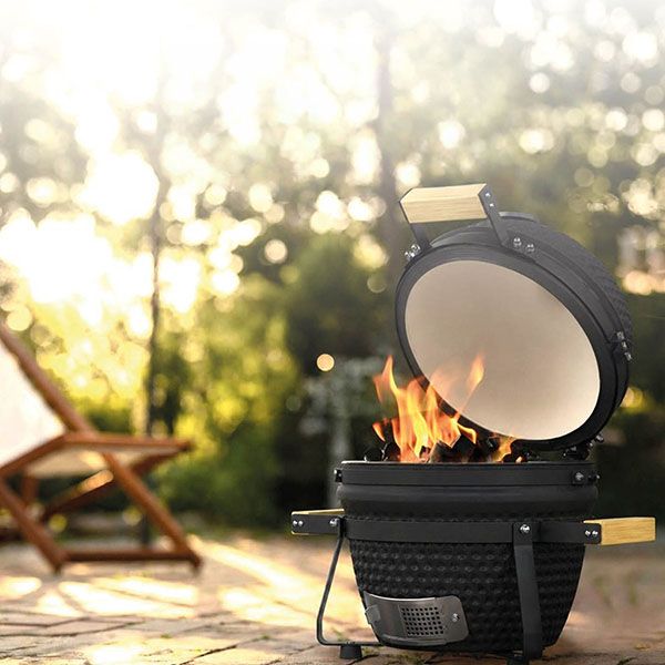 Kamado BBQ met open deksel en brandend vuur in een zonnige tuinsetting.