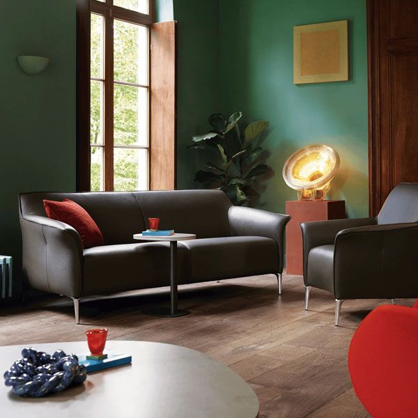 Donkere leren Leolux bank en fauteuil in een sfeervolle woonkamer met groene wand, houten vloer en warme designverlichting.