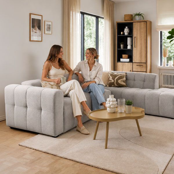 Moderne woonkamer met lichte modulaire hoekbank, ronde salontafel en houten kast in een warm en natuurlijk interieur.