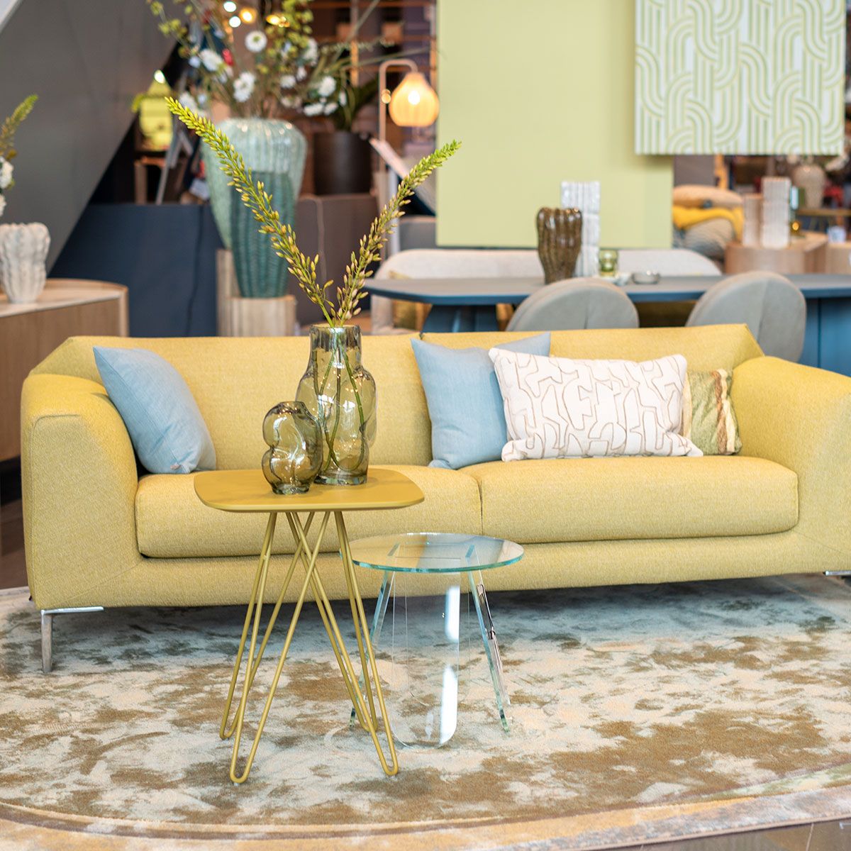 Gele bank met sierkussens, glazen tafels en decoratieve vazen in moderne woonkamer