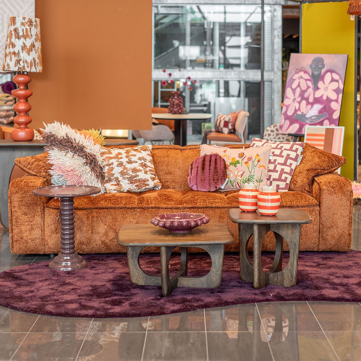 Paarse fluwelen bank met roze kussens in warme woonkamer met oranje wand en bijzettafel