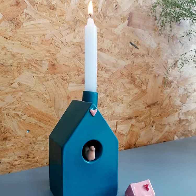 Een blauw keramieken vogelhuisje met een witte kaars