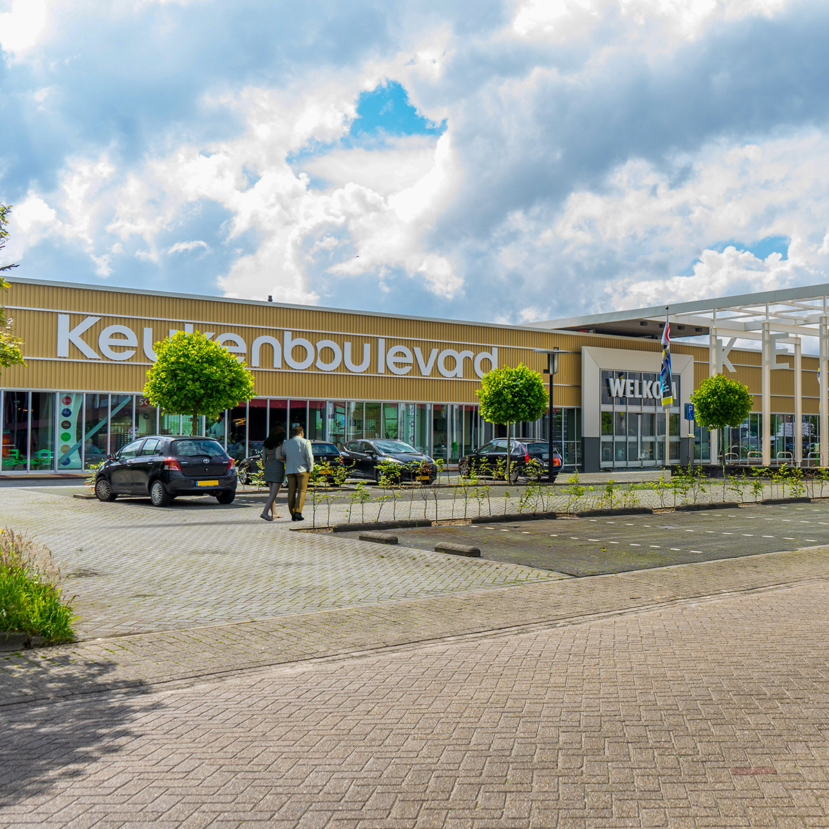 vooraanzicht van het pand van de keukenboulevard in wolvega. Gele gevel met witte letters met een parkeerplaats
