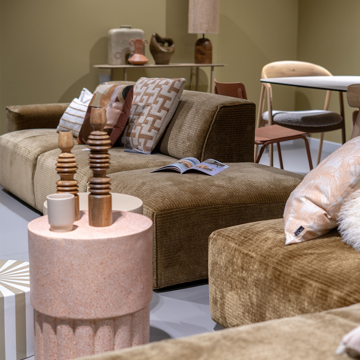 Een donkergroene bank met twee gekleurde kussens een een beige bijzettafel