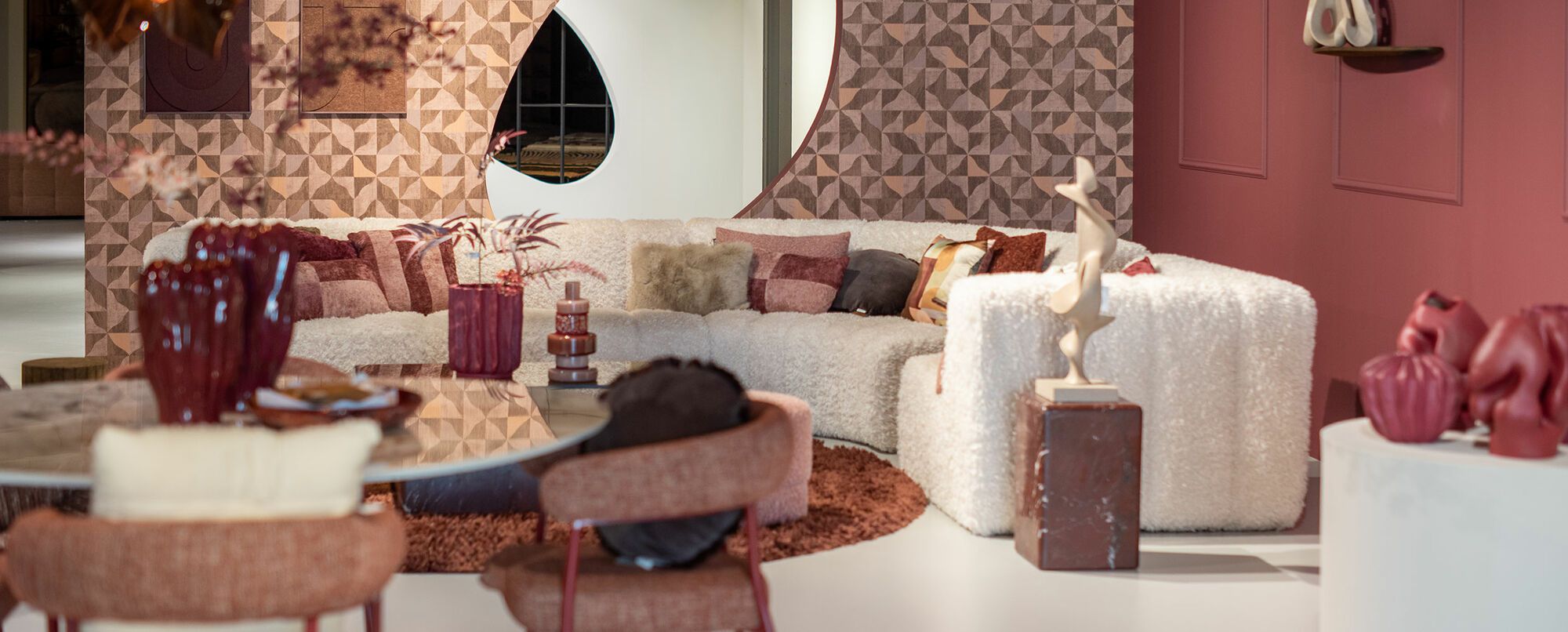 Grote grijze hoekbank met sierkussens op bordeaux vloerkleed en donkere salontafels