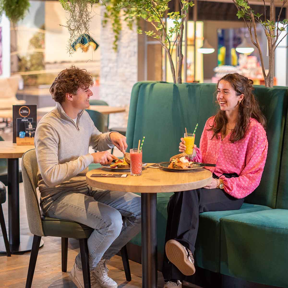 Een jonge man en vrouw eten lunch het restaurant bij Home Center in Wolvega op een groene bank met een rond tafeltje