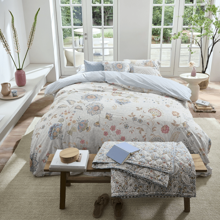 Tweepersoonsbed met bloemenbeddengoed in een lichte slaapkamer met grote ramen en uitzicht op de tuin.