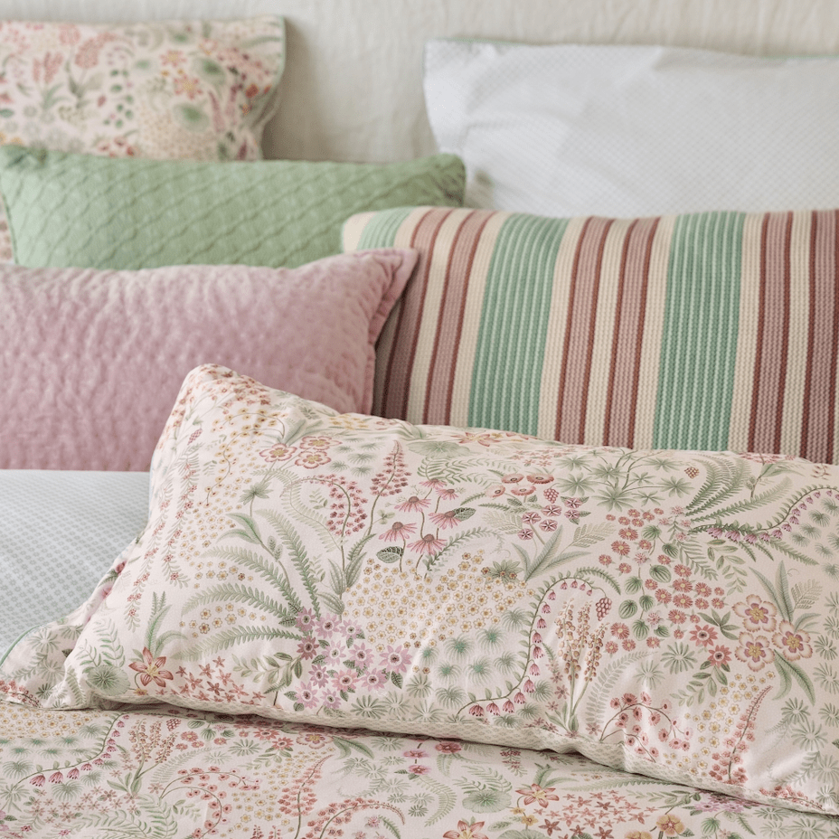 Sierkussens en beddengoed met bloemenprint in zachte roze- en groentinten op een stijlvol opgemaakt bed.