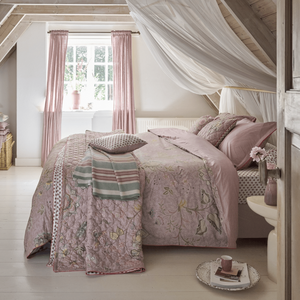 Roze bloemenbeddengoed met sierkussens en sprei in een landelijke slaapkamer met hemelbed.