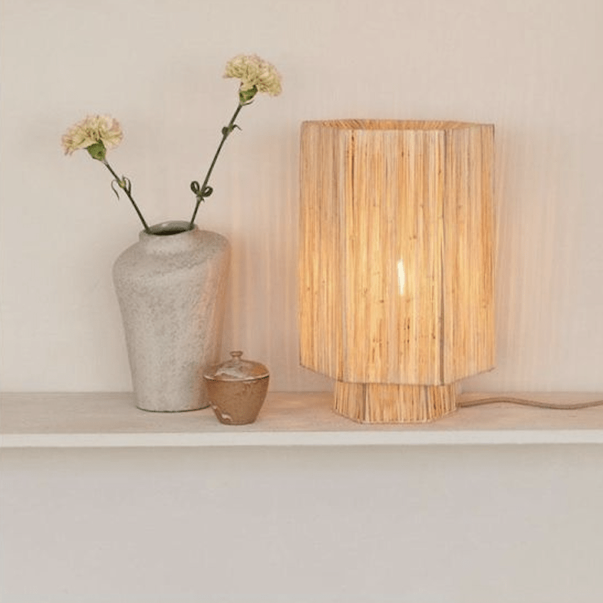 Houten tafellamp met warme verlichting naast een keramische vaas met bloemen op een wandplank.